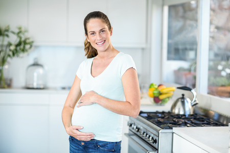 Portrait of happy pregnant woman standing in kitchenの写真素材