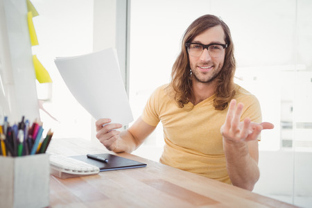 Portrait of happy hipster gesturing while holding documents at desk in officeの写真素材