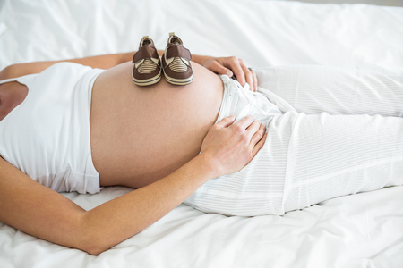 High angle view of baby shoes on pregnant woman belly in bedroomの写真素材