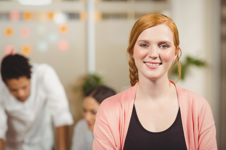 Portrait of smiling businesswoman standing with arms crossed while colleagues working in backgroundの写真素材