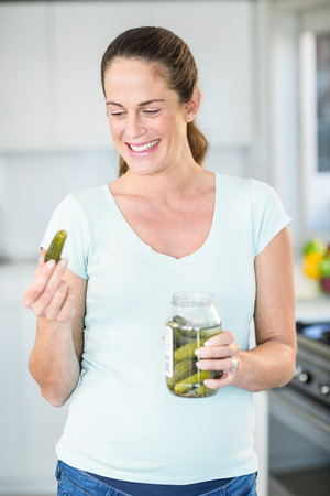 Happy pregnant woman looking at pickle in kitchenの写真素材