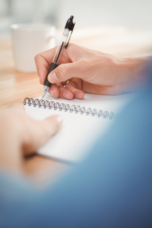 Cropped image of businessman writing on spiral book at desk in officeの写真素材