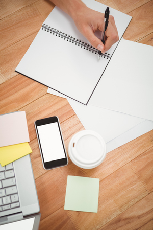 Businessman writing on spiral notebook at desk in officeの写真素材