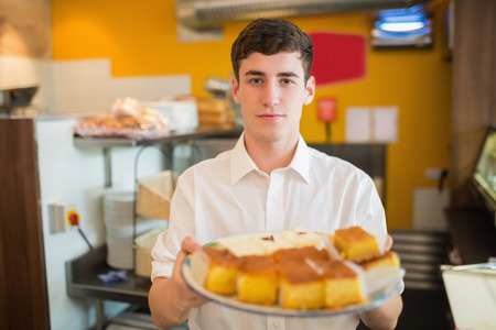 Portrait of male worker with pastries standing in bakeryの写真素材