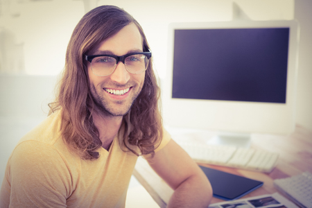 Portrait of happy hipster wearing eye glasses at desk in officeの写真素材