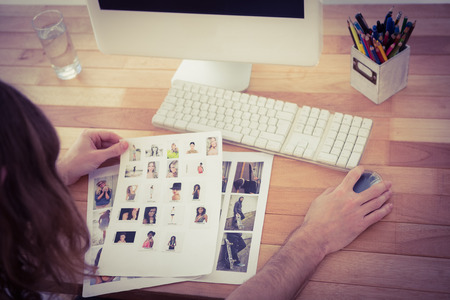 High angle view of hipster holding photographs working at computer desk in officeの写真素材