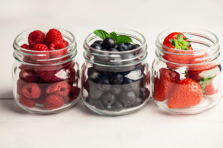 Glass jars of fresh berries on wooden tableの写真素材