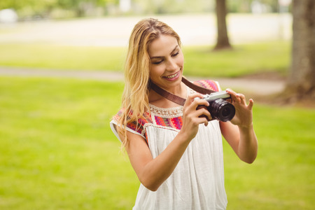 Smiling woman looking at digital camera while standing on grass in parkの写真素材