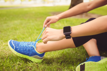 Low section of woman tying shoelace while sitting on grass in parkの写真素材