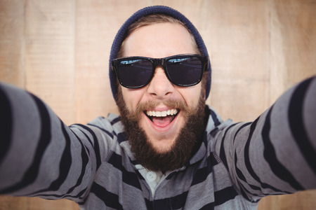 Portrait of happy hipster wearing sunglasses against wooden backgroundの写真素材