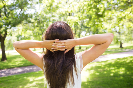 Rear view of woman with hands behind head while standing in parkの写真素材