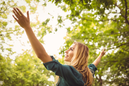 Beautiful smiling woman with arms raised while standing in parkの写真素材