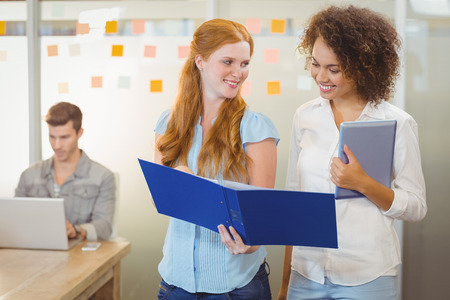 Happy Businesswomen looking at document with male colleague working in background at office