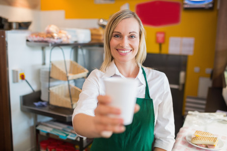 Portrait of happy female shop owner holding glass in bakeryの写真素材