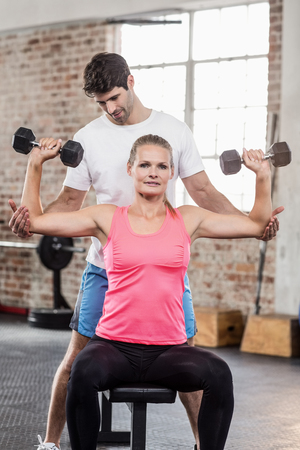 Fit woman lifting dumbbells with trainer in crossfit gymの写真素材