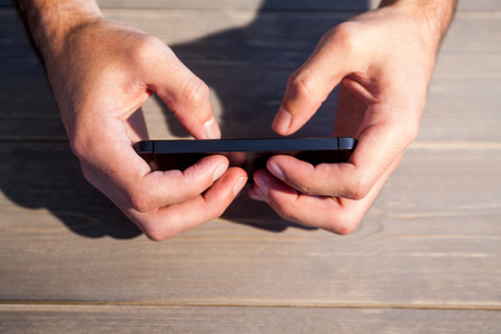 Person holding smartphone at wooden deskの写真素材