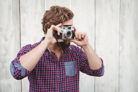 Hipster photographing with camera against wooden fenceの写真素材