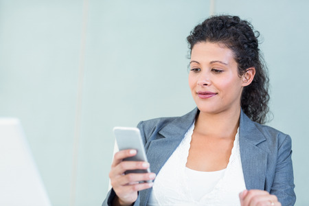 Smiling businesswoman using smart phone while working in officeの写真素材