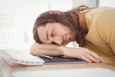Hipster resting head at computer desk in officeの写真素材