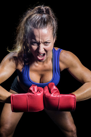 Portrait of aggressive female fighter flexing muscles against black backgroundの写真素材