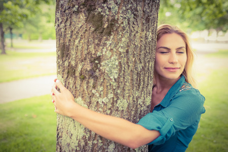 Smiling woman with eyes closed while hugging tree in parkの写真素材