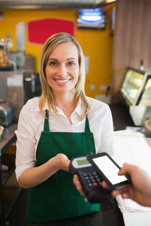 Portrairt of female worker accepting payment from customer through NFC in bakeryの写真素材