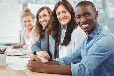 Portrait of smiling business people sitting in row at desk in office