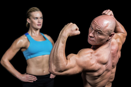 Muscular man flexing muscles in front of instructor against black backgroundの写真素材