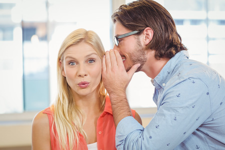 Businesswoman listening to rumor which male colleague is whispering into her ear