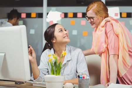 Happy businesswomen using computer in office with male colleague working in backgroundの写真素材