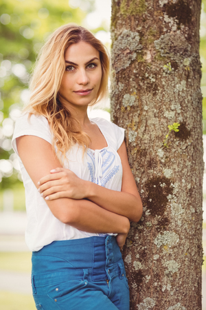 Beautiful woman with arms crossed standing by tree in parkの写真素材