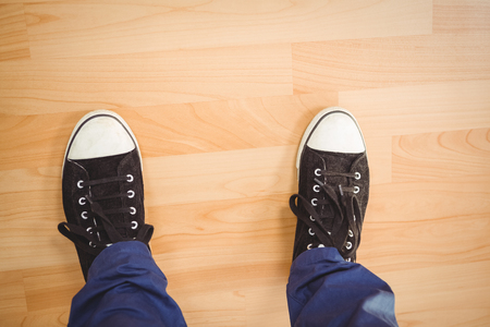 Low section of businessman wearing canvas shoes standing on hardwood floor