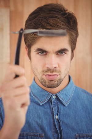 Portrait of hipster holding straight edge razor against wooden wallの写真素材
