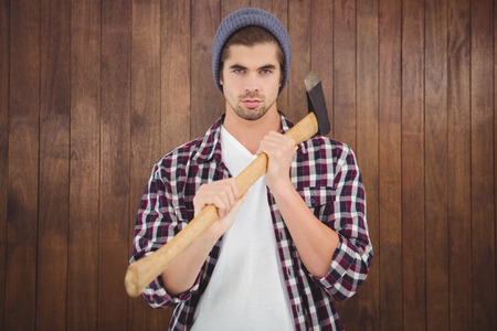 Portrait of confident man holding axe on shoulder while standing against wooden wallの写真素材