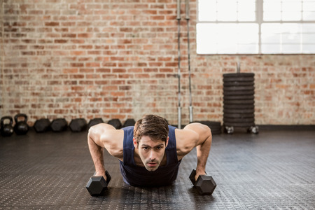 Man doing push up holding dumbbell at the gym