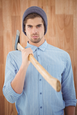 Portrait of serious hipster holding axe on shoulder while standing against wooden wallの写真素材