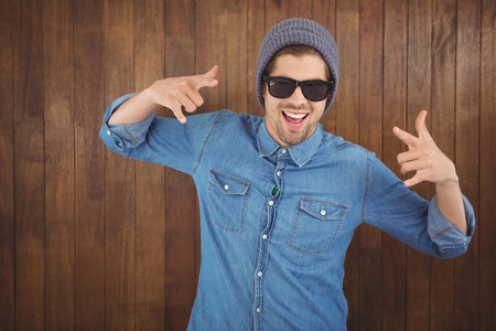 Happy hipster showing rock and roll hand sign against wooden wallの写真素材