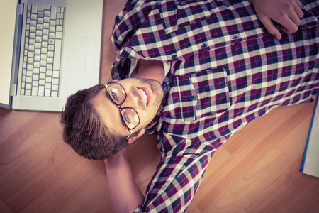 Portrait of happy hipster wearing eye glasses lying on hardwood floor at officeの写真素材