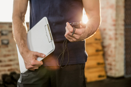 Midsection of trainer holding clipboard and stopwatch at the gym