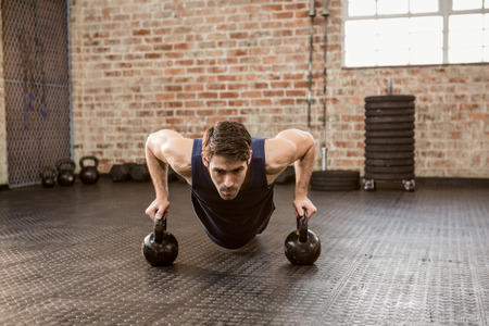 Man doing push ups holding kettlebell at the gymの写真素材