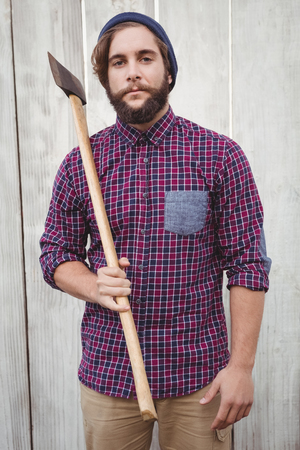 Portrait of hipster holding axe against wooden fenceの写真素材