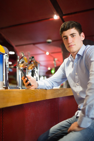 Portrait of confident man holding mobile phone while sitting at bar counterの写真素材