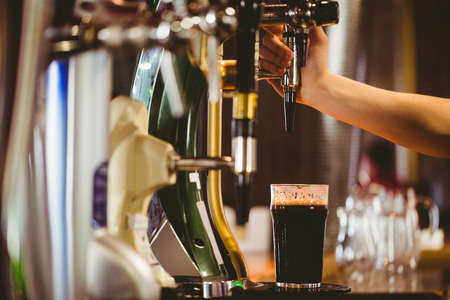 Cropped hand of bartender dispensing beer at bar counterの写真素材