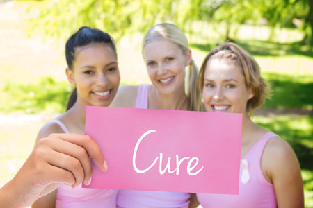The word cure and hand holding card against smiling women in pink for breast cancer awarenessの写真素材