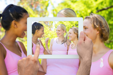 Hand holding tablet pc against smiling women in pink for breast cancer awarenessの写真素材