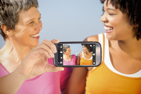 Hand holding smartphone showing against two sporty women smiling at each otherの写真素材