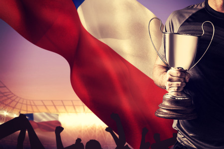 Midsection of successful rugby player holding trophy and ball against large football stadium under purple skyの写真素材