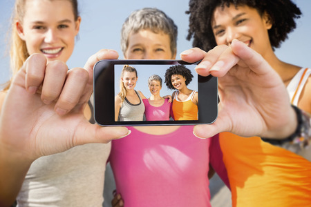Hand holding smartphone showing against sporty women smiling at camera