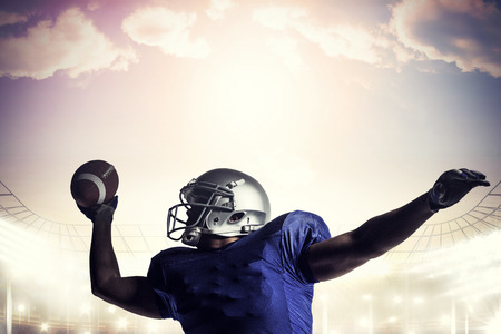American football player throwing ball against rugby stadiumの写真素材