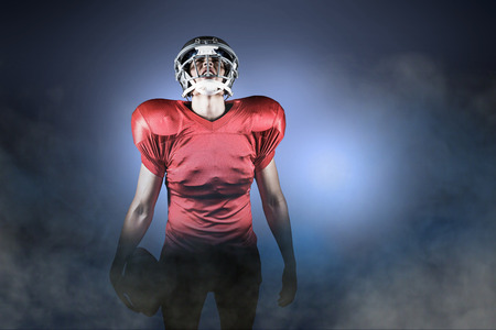 American football player holding ball while looking up against cloudy skyの写真素材